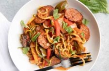Close view of sausage and peppers served with zoodles on a round white plate.