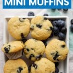 Overhead of a square white plate with mini blueberry muffins and fresh berries. A text overlay reads, "Blueberry Mini Muffins."