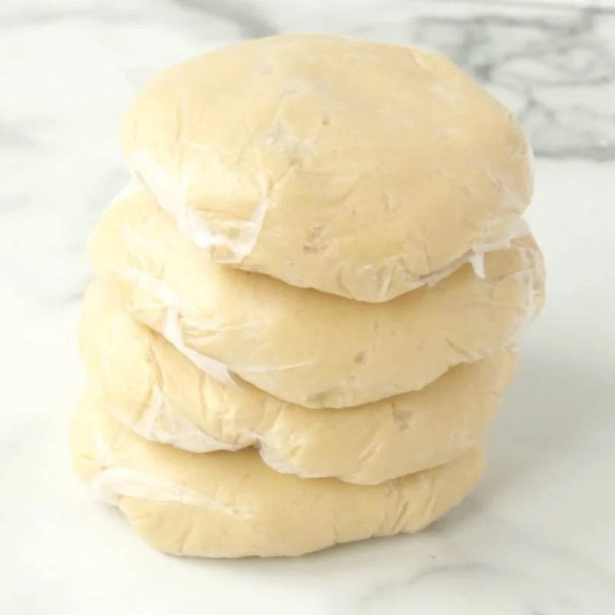 Four discs of sugar cookie dough wrapped in plastic wrap stacked on a countertop