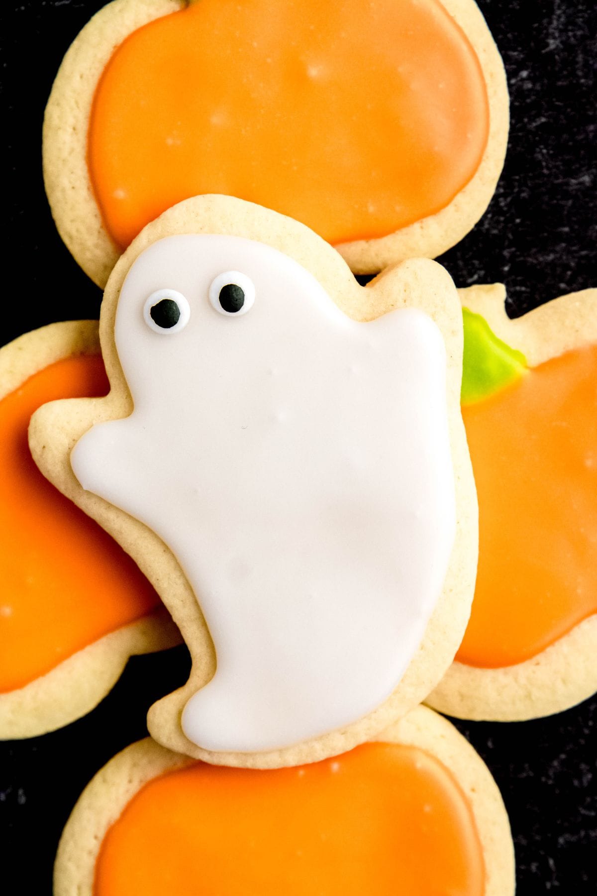 A Halloween sugar cookie decorated like a ghost sits on top of cookies decorated like pumpkins