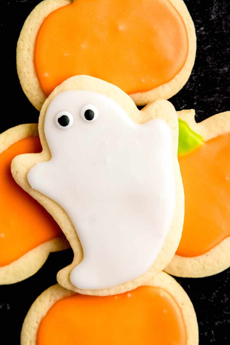 A ghost sugar cookie rests atop four cookies decorated like pumpkins.