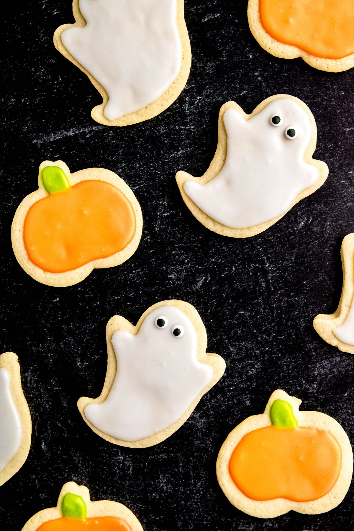 Halloween sugar cookies decorated like ghosts and pumpkins rest on a black background