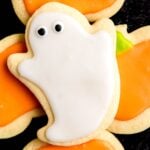A Halloween sugar cookie decorated like a ghost sits on top of cookies decorated like pumpkins