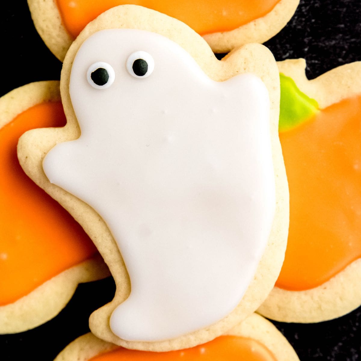 A Halloween sugar cookie decorated like a ghost sits on top of cookies decorated like pumpkins