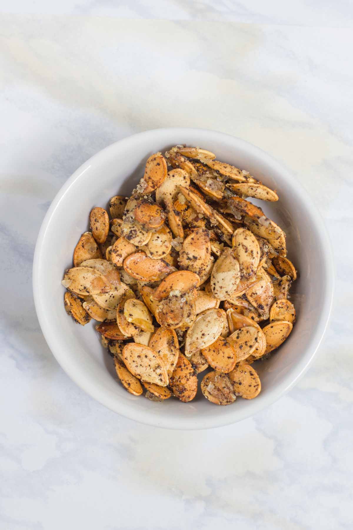 Seasoned roasted pumpkin seeds in a white bowl on a white marble countertop