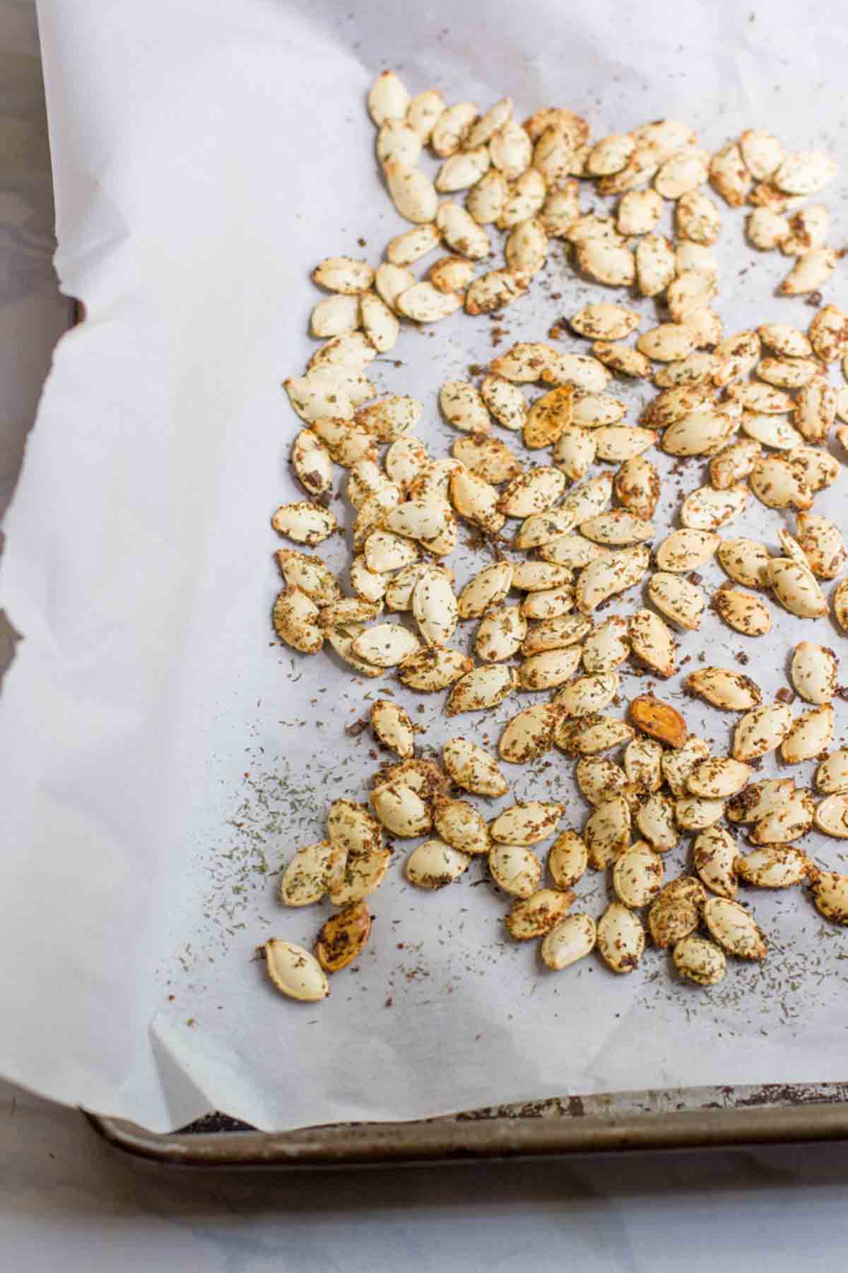 Homemade roasted pumpkin seeds with seasoning on a parchment lined baking sheet.