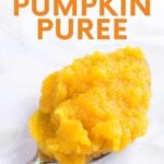 Close view of a heaping spoonful of orange colored puree resting on a marble counter. A text overlay reads, "Homemade Pumpkin Puree."