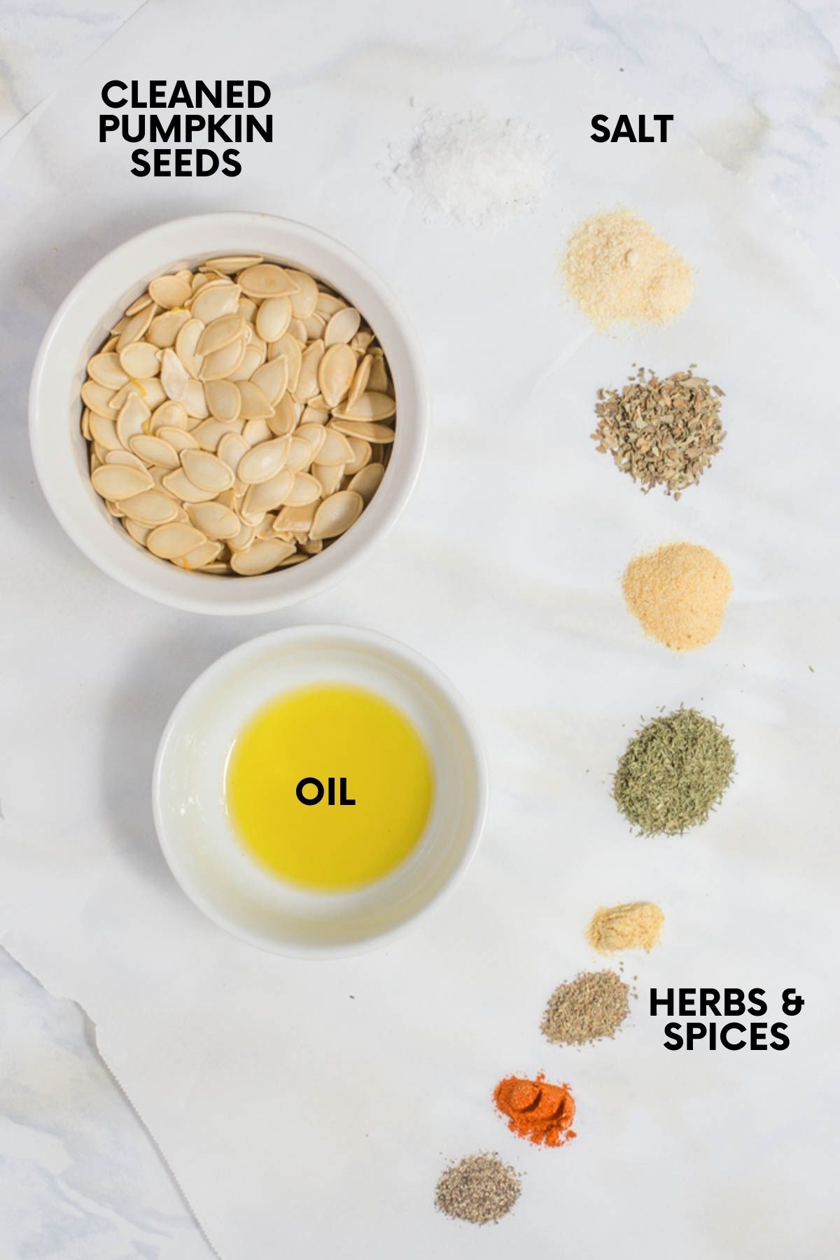 Ingredients for roasted pumpkin seeds in bowls on a white countertop: cleaned pumpkin seeds, oil, salt, and herbs and spices