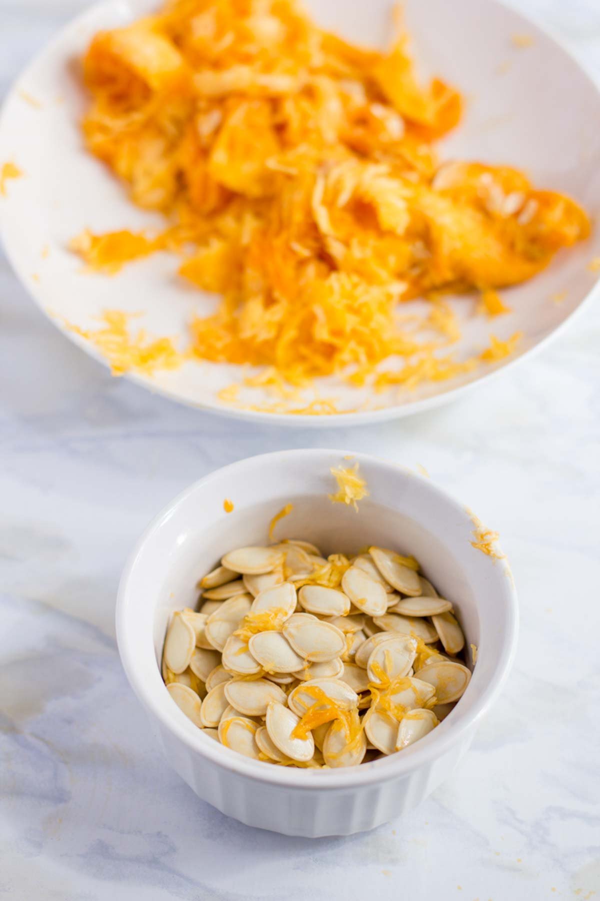 Pumpkin seeds directly scooped out of pumpkin in a white bowl on a white countertop