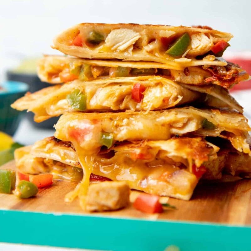 Finished version of my chicken quesadillas recipe stacked on top of a wooden cutting board.