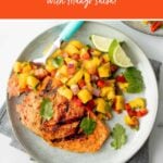 Overhead of fork loaded with a bite of grilled salmon and mango salsa on a plate beside finished salmon and salsa. A text overlay reads, "Grilled Salmon with Mango Salsa!"