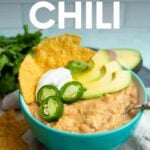 A teal bowl filled with Instant Pot white chili topped with sour cream, avocado, jalapeno, and corn tortilla chips. A text overlay reads, "Instant Pot White Chicken Chili."