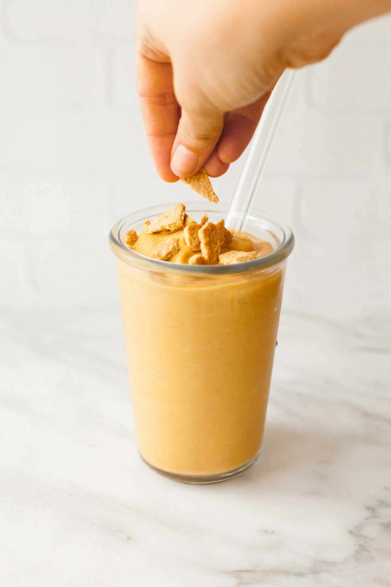 A hand garnishes a smoothie with graham crackers