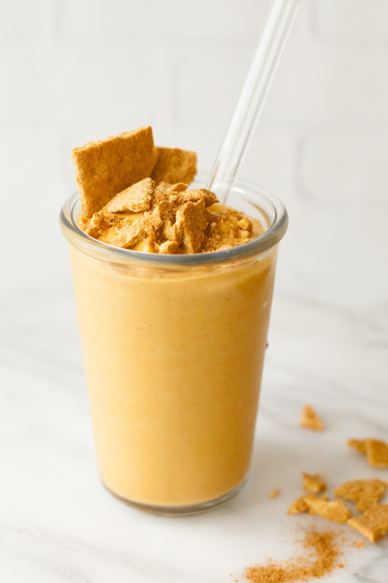Pumpkin smoothie in a clear glass with a glass straw