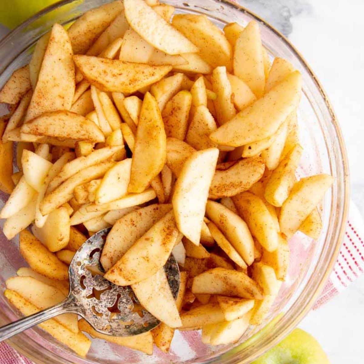 A metal spoon tosses apple slices with seasonings