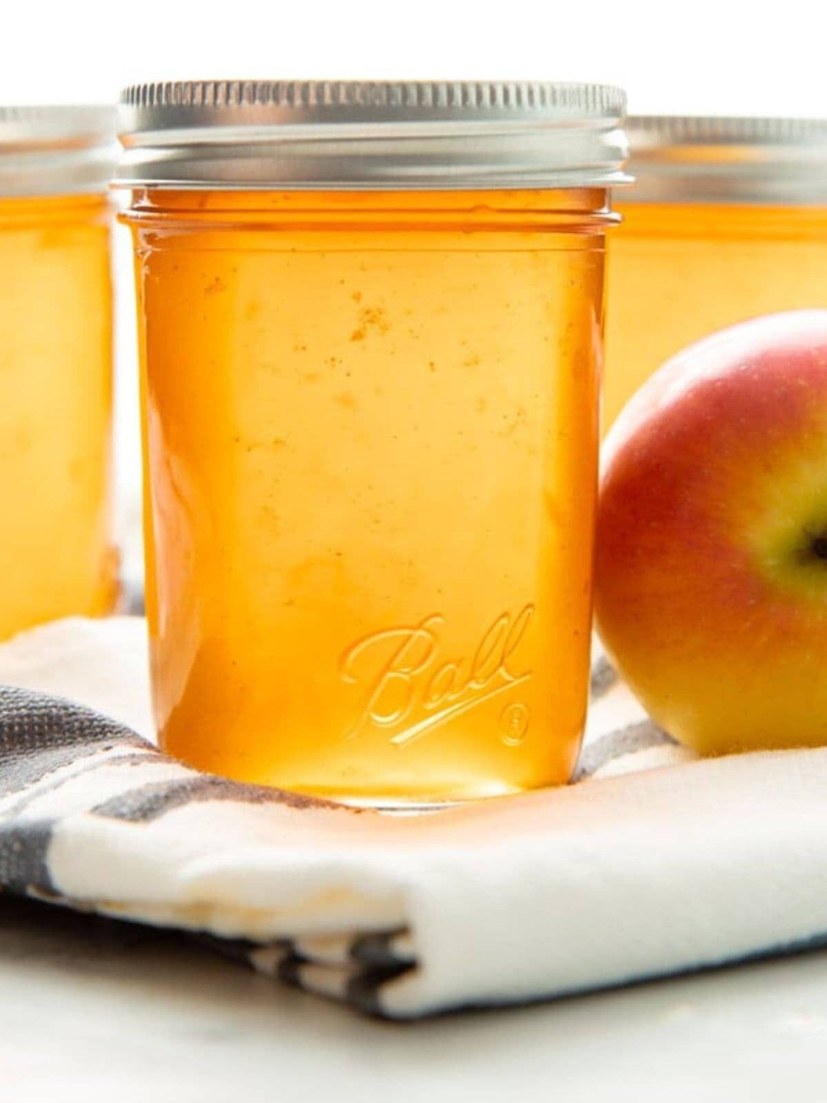 Three jars of apple jelly sit on a white countertop