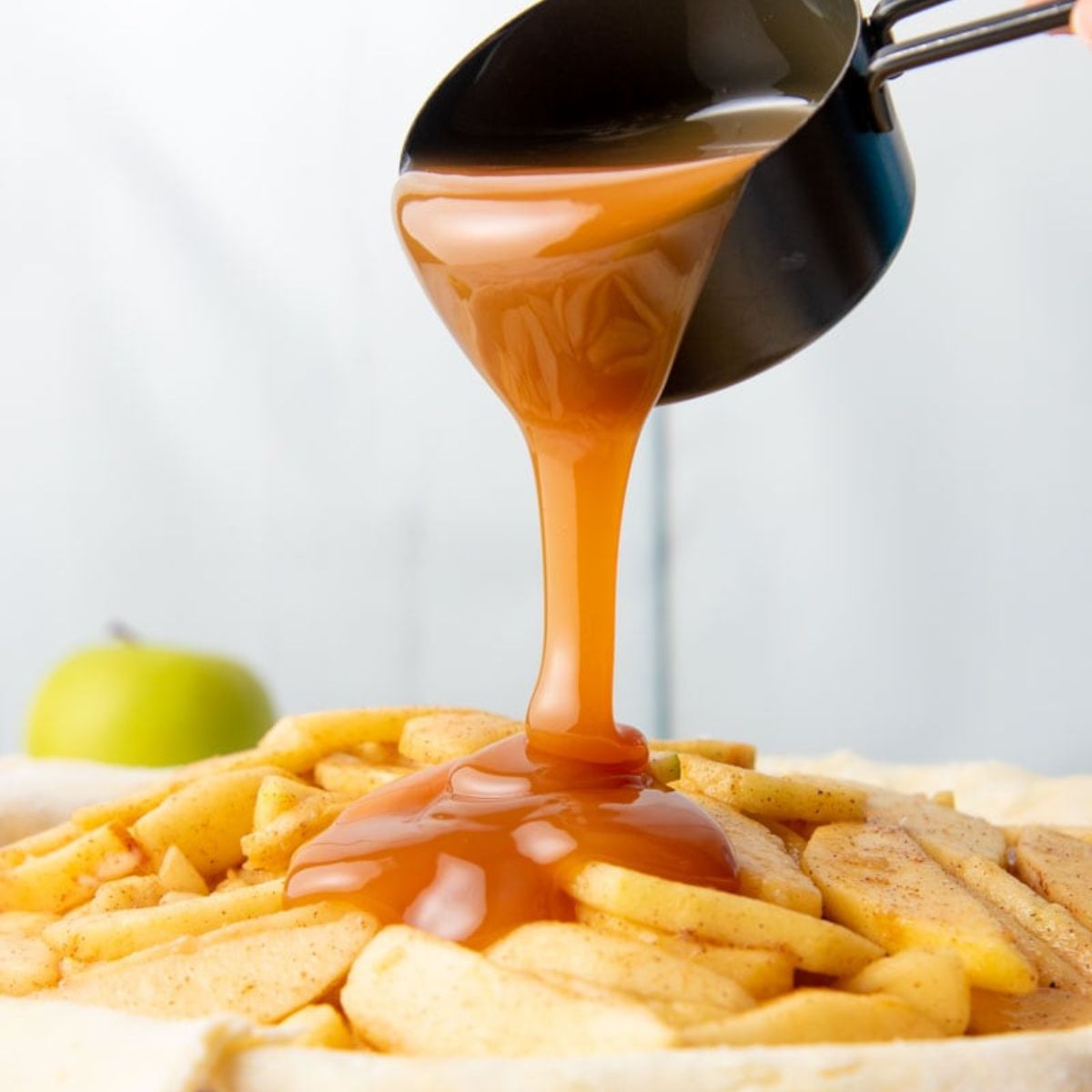 A measuring cup pours caramel over sliced apples