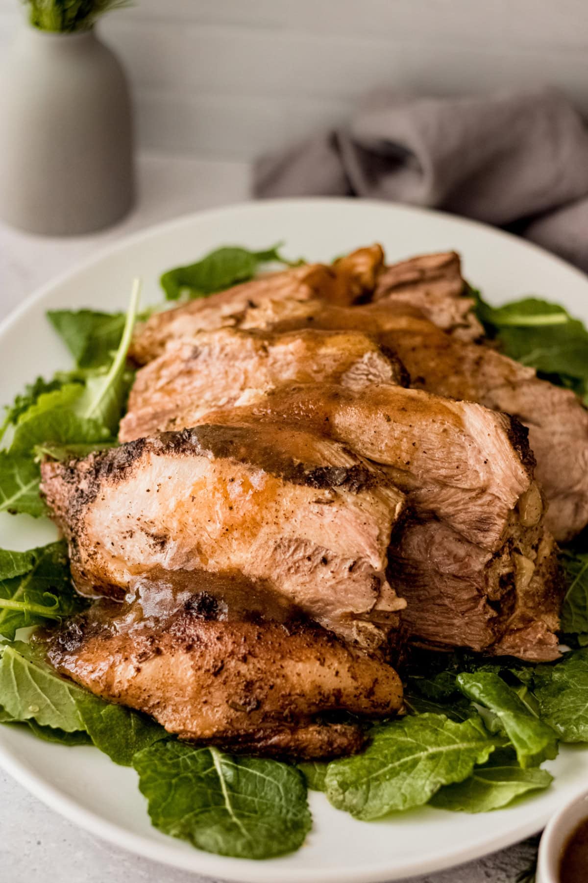Instant Pot pork roast, sliced and topped with sauce, on a bed of greens.