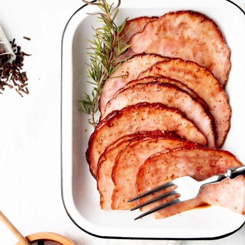Slow cooker honey glazed ham sliced on a white enameled platter with a serving fork.
