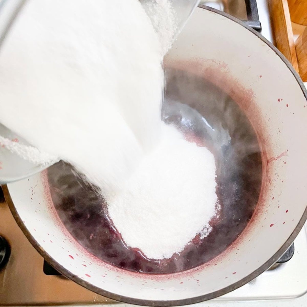 Sugar pours into a pot of hot pomegranate juice.