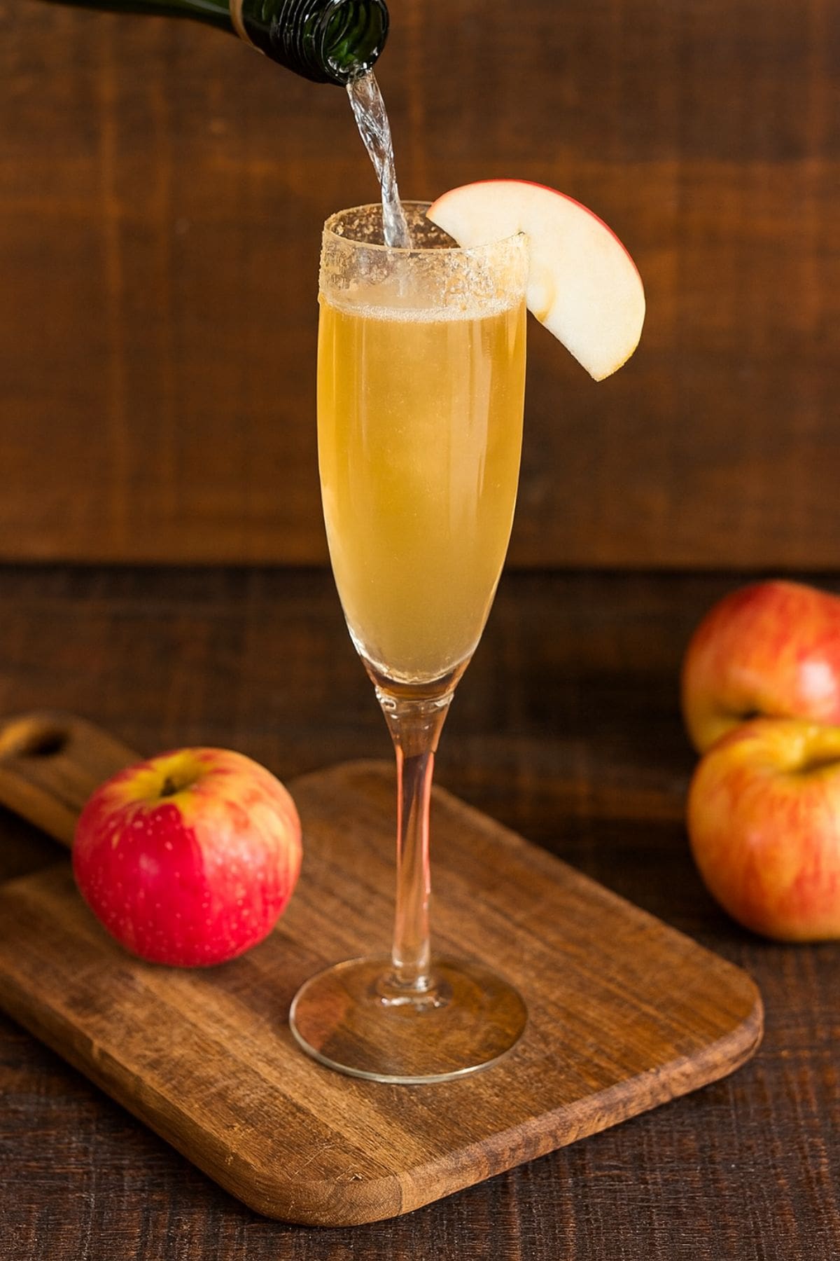 Champagne pours into a flute of cider garnished with an apple slice