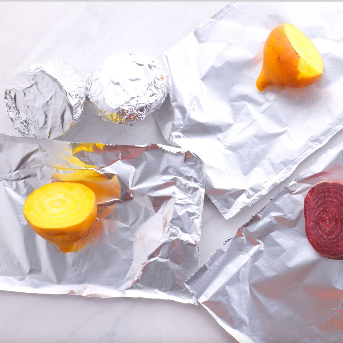 Trimmed beets on pieces of aluminum foil, ready to be wrapped.