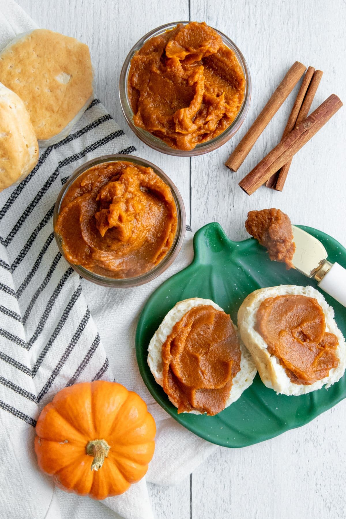 Split biscuit spread with pumpkin butter on a green pumpkin-shaped plate. There are two jars of pumpkin butter nearby.
