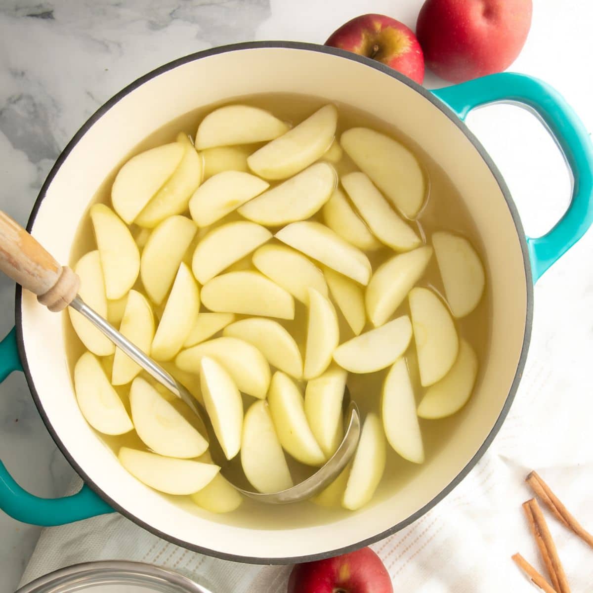 A ladle rests in a pot of blanching apple slices.