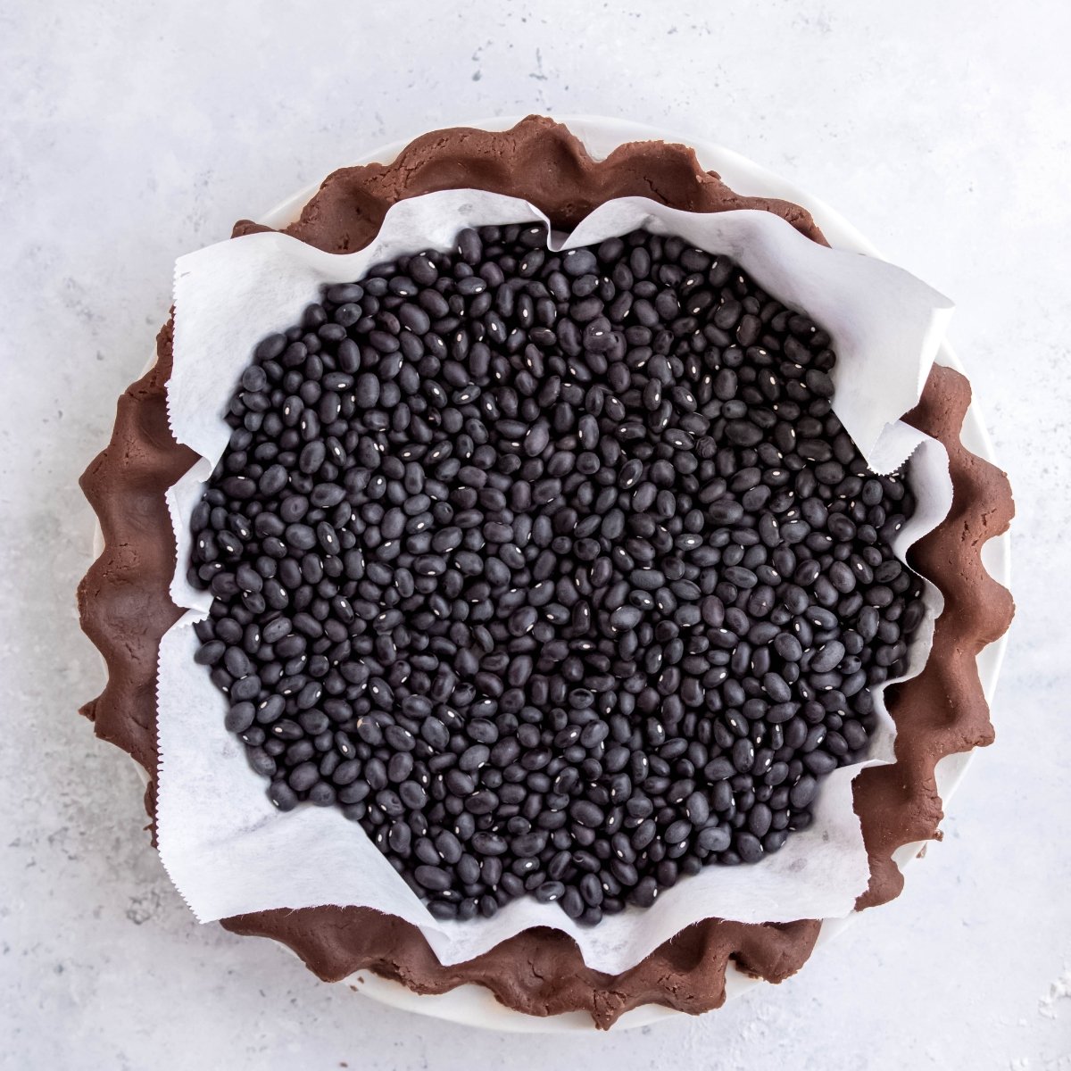 Beans on top of parchment paper inside a chocolate pie crust, ready for blind baking.