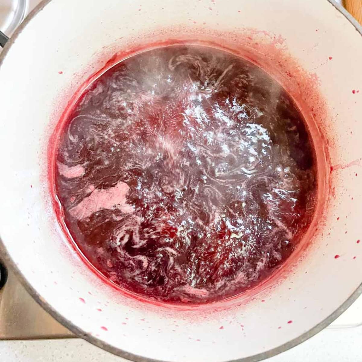 Pomegranate jelly comes to a boil in a white pot.