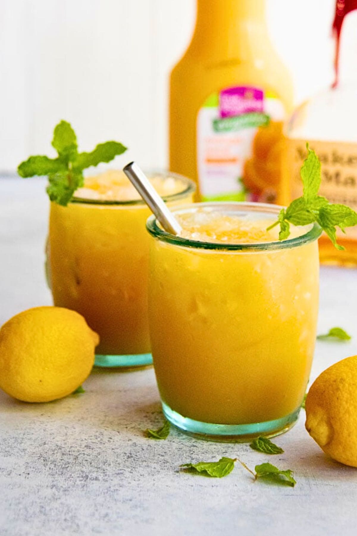 Two glasses of orange whiskey punch with mint sprig garnishes.