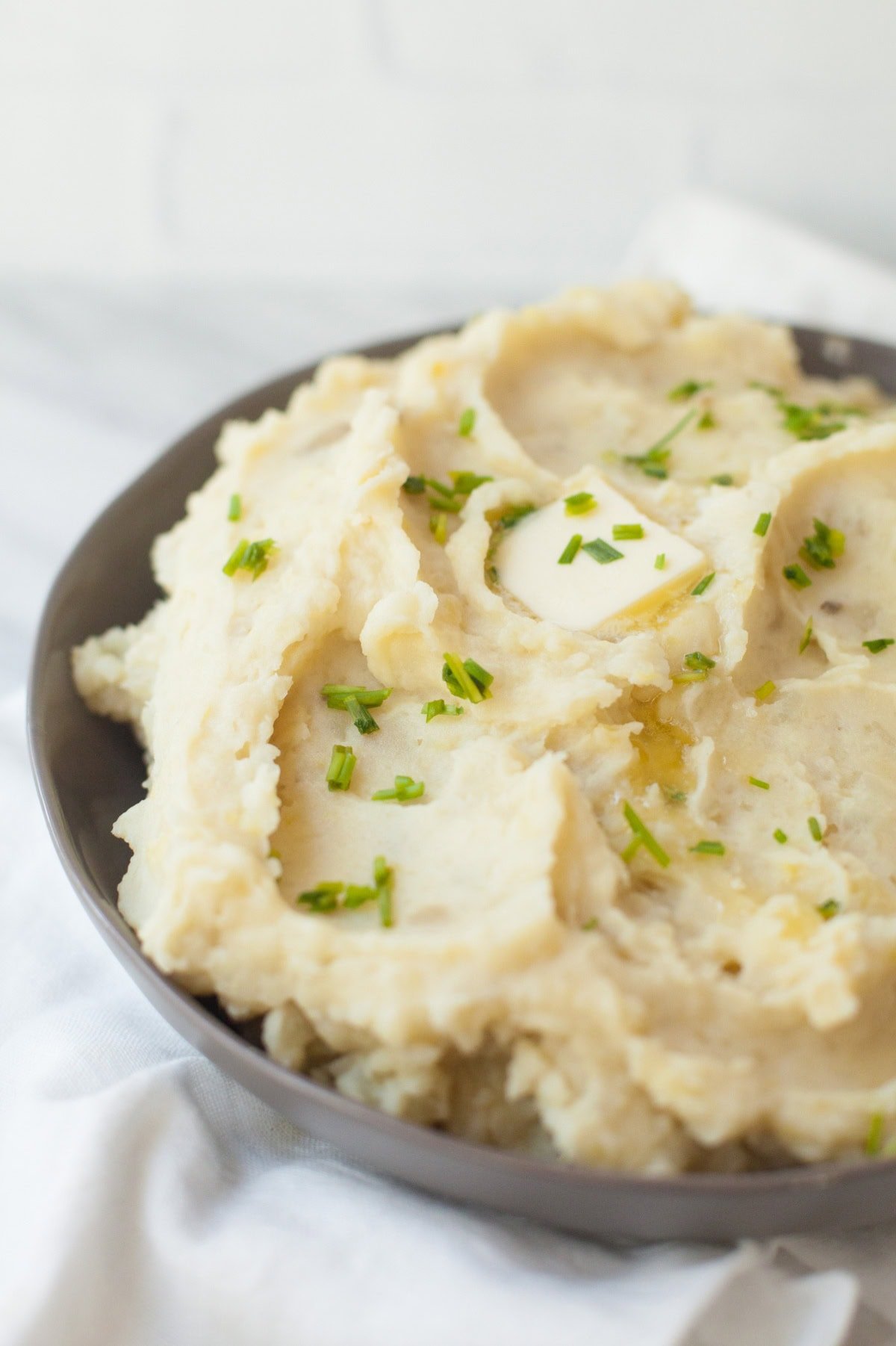 Mashed potatoes topped with butter and chopped chives, in a gray bowl.