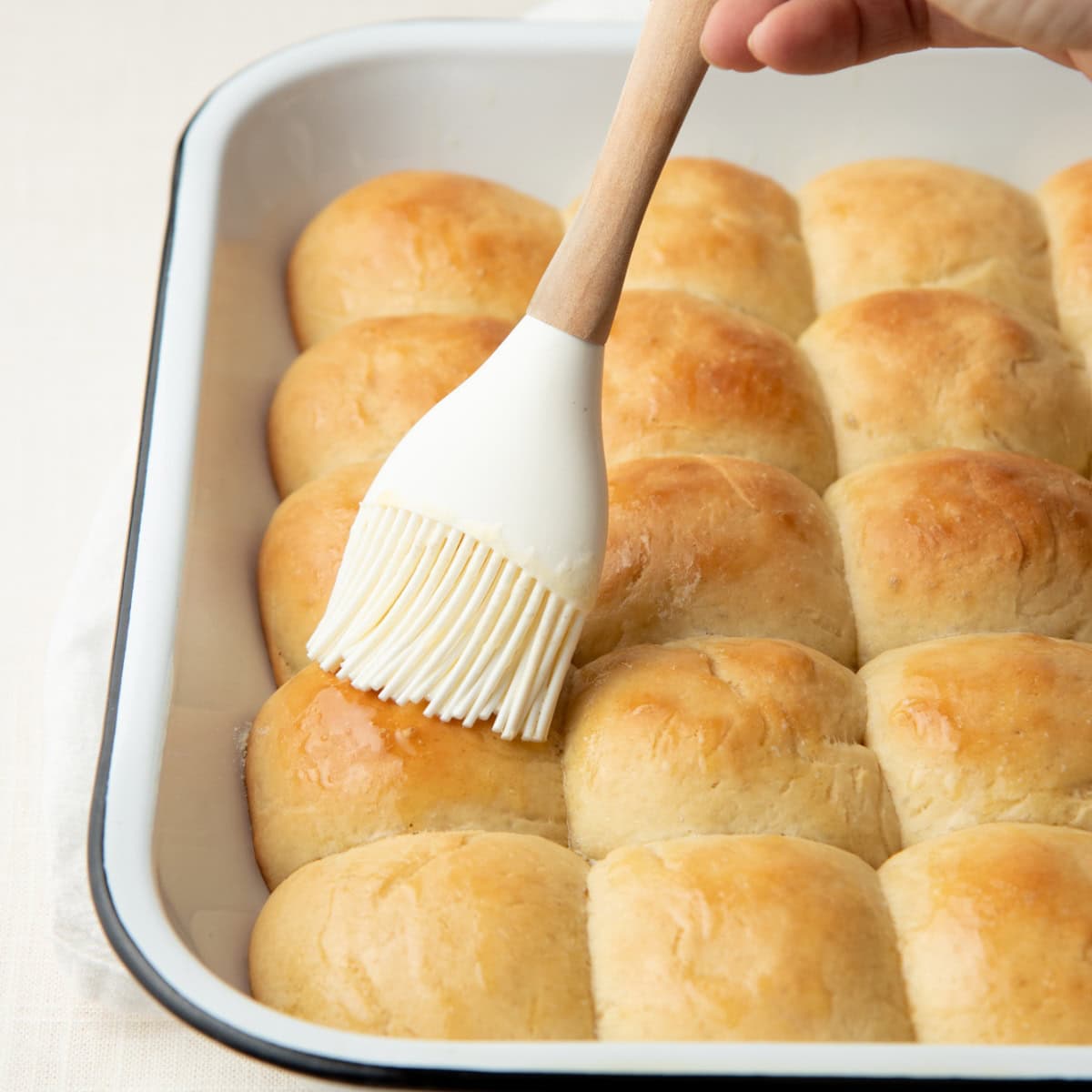 A pastry brush spreads melted butter over the top of easy yeast rolls.