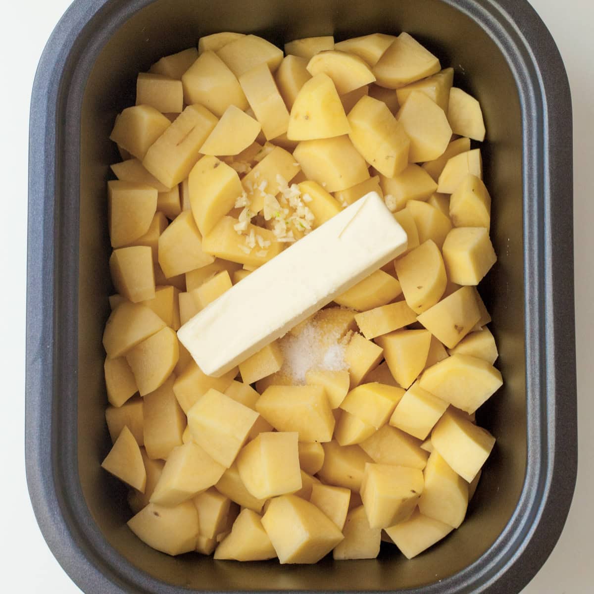 Butter, garlic, and salt on top of chopped potatoes in the basin of a slow cooker.