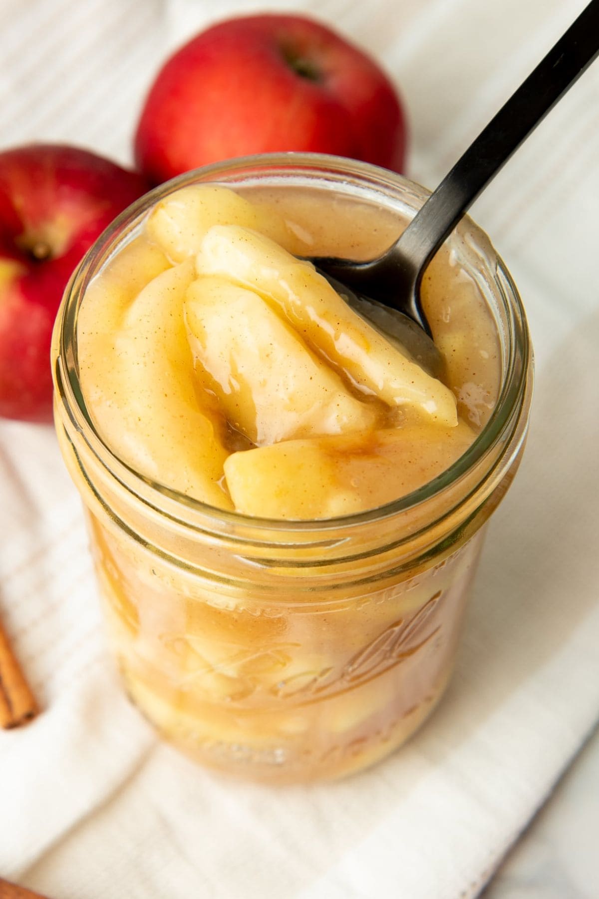 A spoon dips into a jar of canned apple pie filling.
