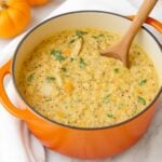 Wooden spoon in an orange soup pot of chicken and pumpkin soup.