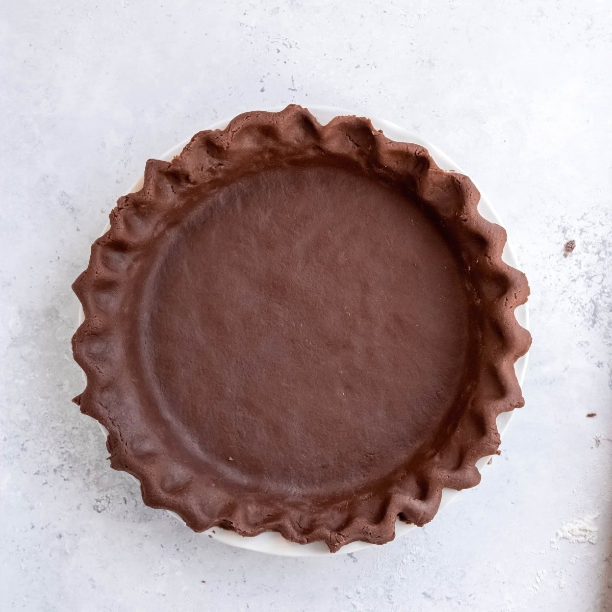 Chocolate pie dough pressed into a pie pan, with fluted edges.