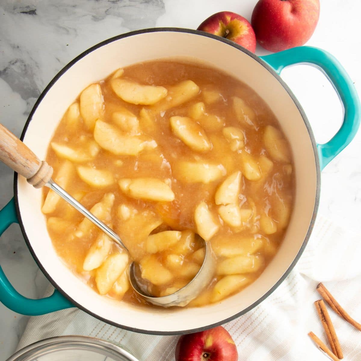 A ladle dips into a blue pot of apple pie filling for canning.