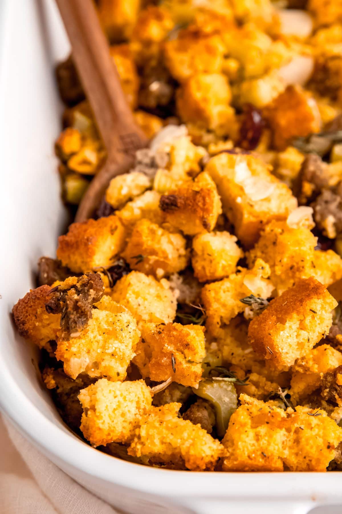 Cornbread sausage dressing with a wooden spoon dug into it.