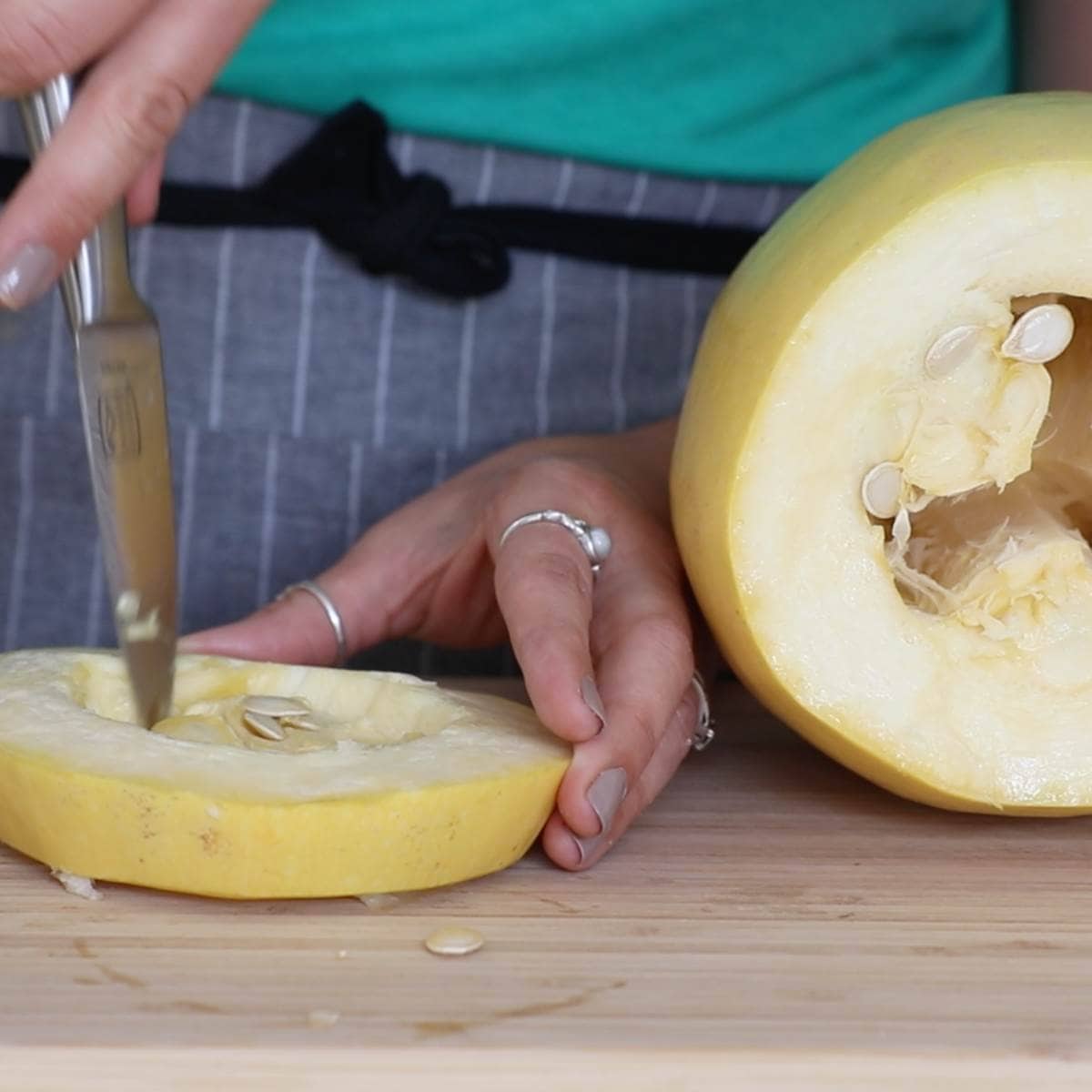 A knife cuts the seeds out of a slice of spaghetti squash
