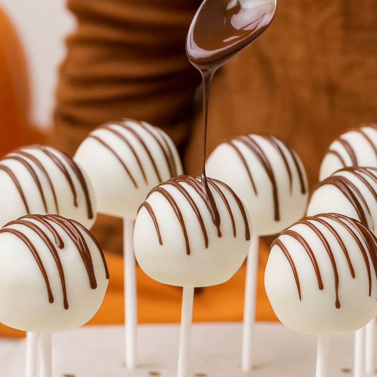 A spoon drizzles chocolate over finished cake pops