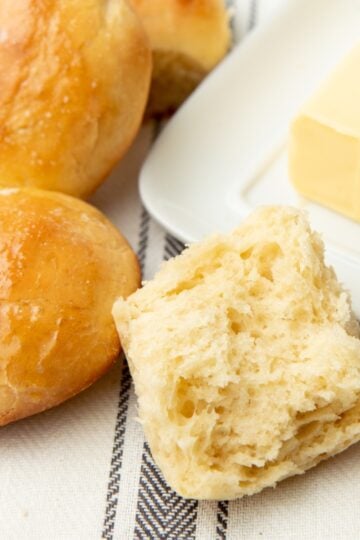A yeast roll split in half next to a butter dish and two whole rolls.