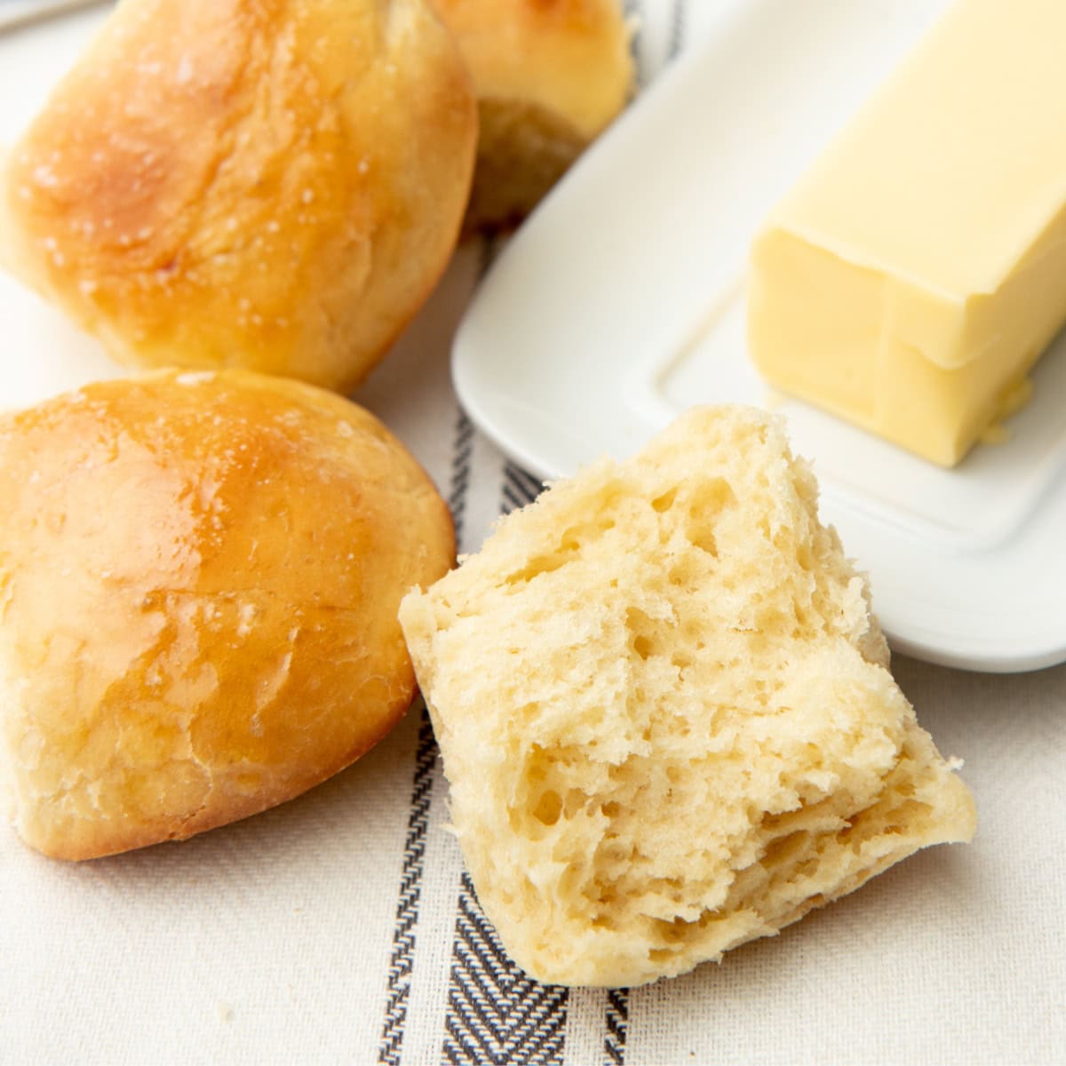 A yeast roll split in half next to a butter dish and two whole rolls.