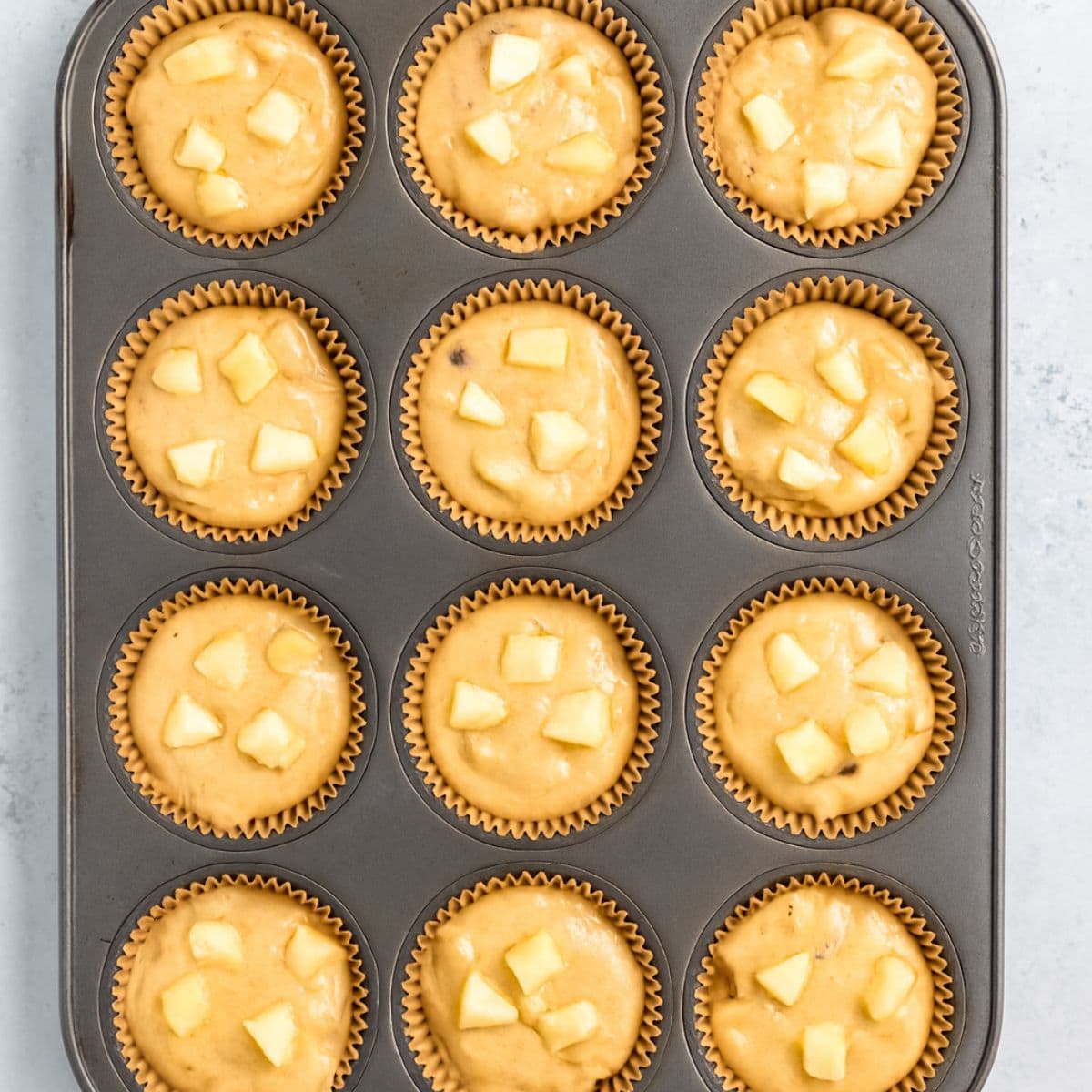 Muffin tin lined with papers and filled with apple cinnamon muffin batter.