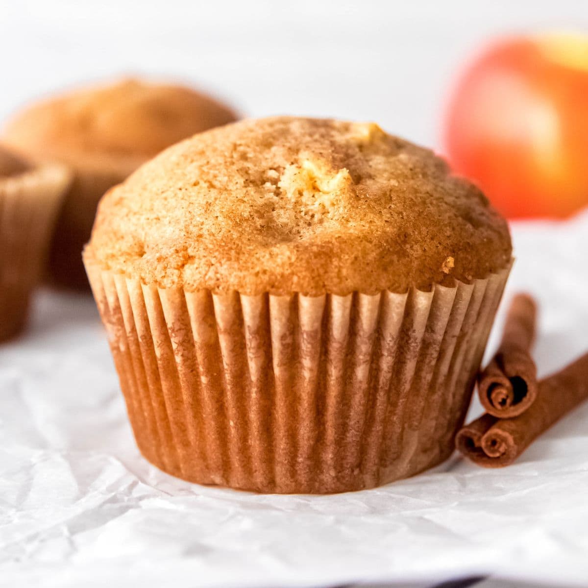 A baked apple cinnamon muffin next to two cinnamon sticks.