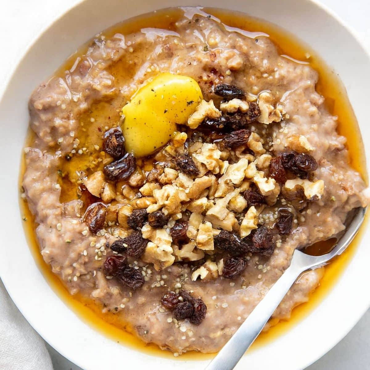 White bowl of oatmeal topped with ghee, raisins, and nuts.