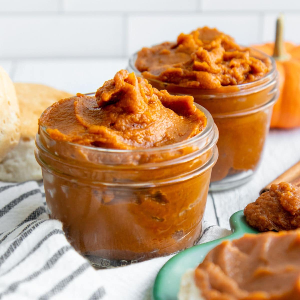 Two jars of pumpkin butter on a striped dishtowel