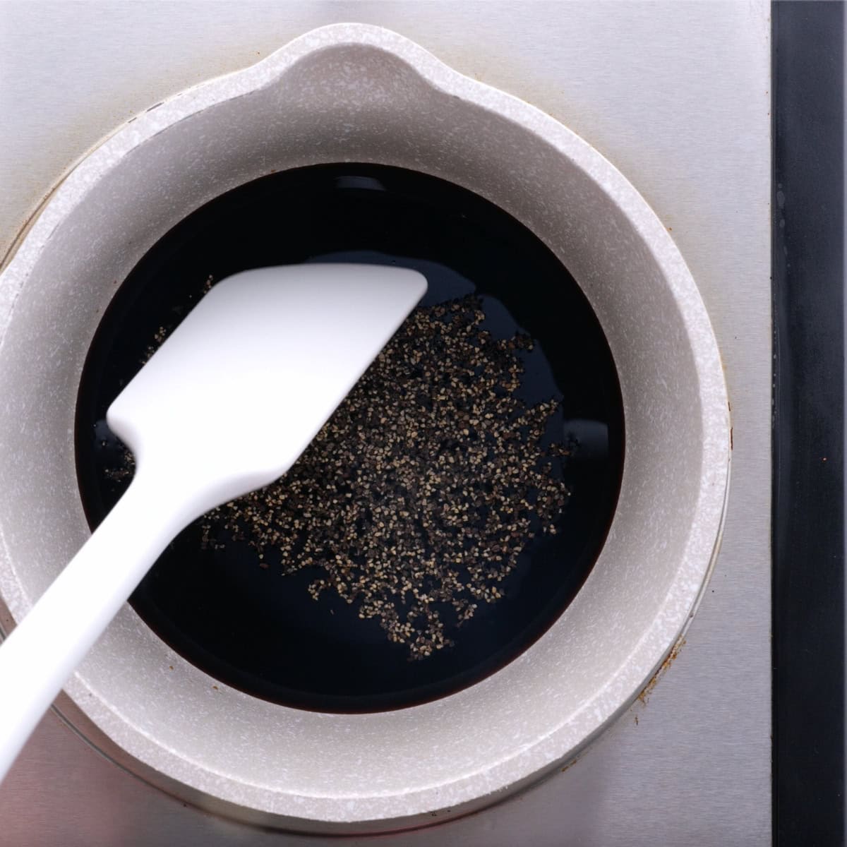 A white plastic spatula in a pot of balsamic glaze.