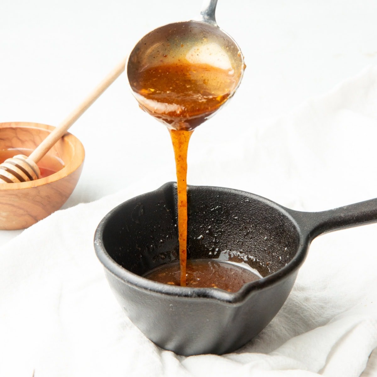 A ladle pours honey mustard glaze into a small pot.