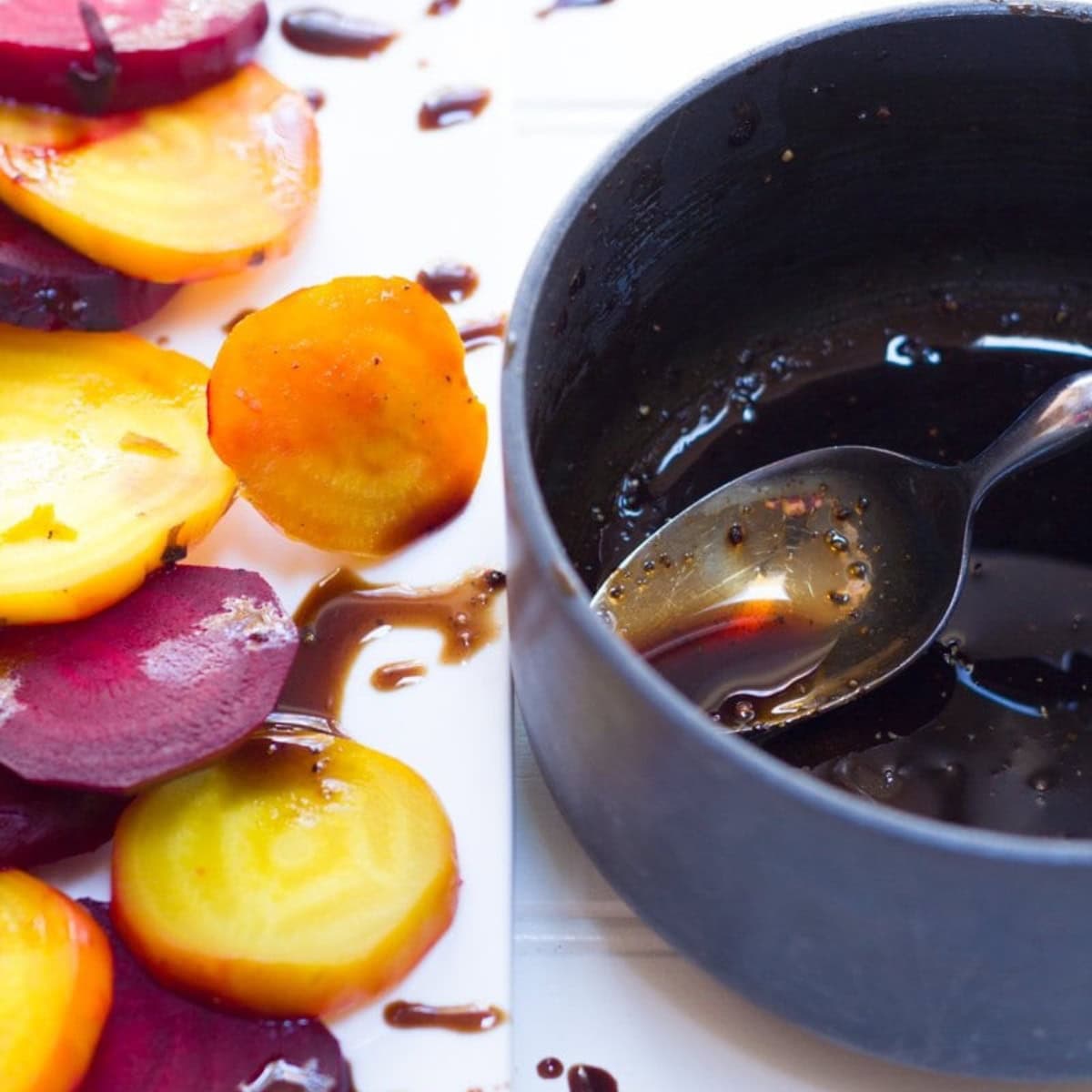 A spoon in a pot of balsamic glaze next to a platter of roasted beets.